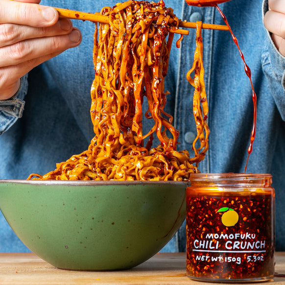 a bowl of noodles lifted by chopsticks covered in chili crunch.