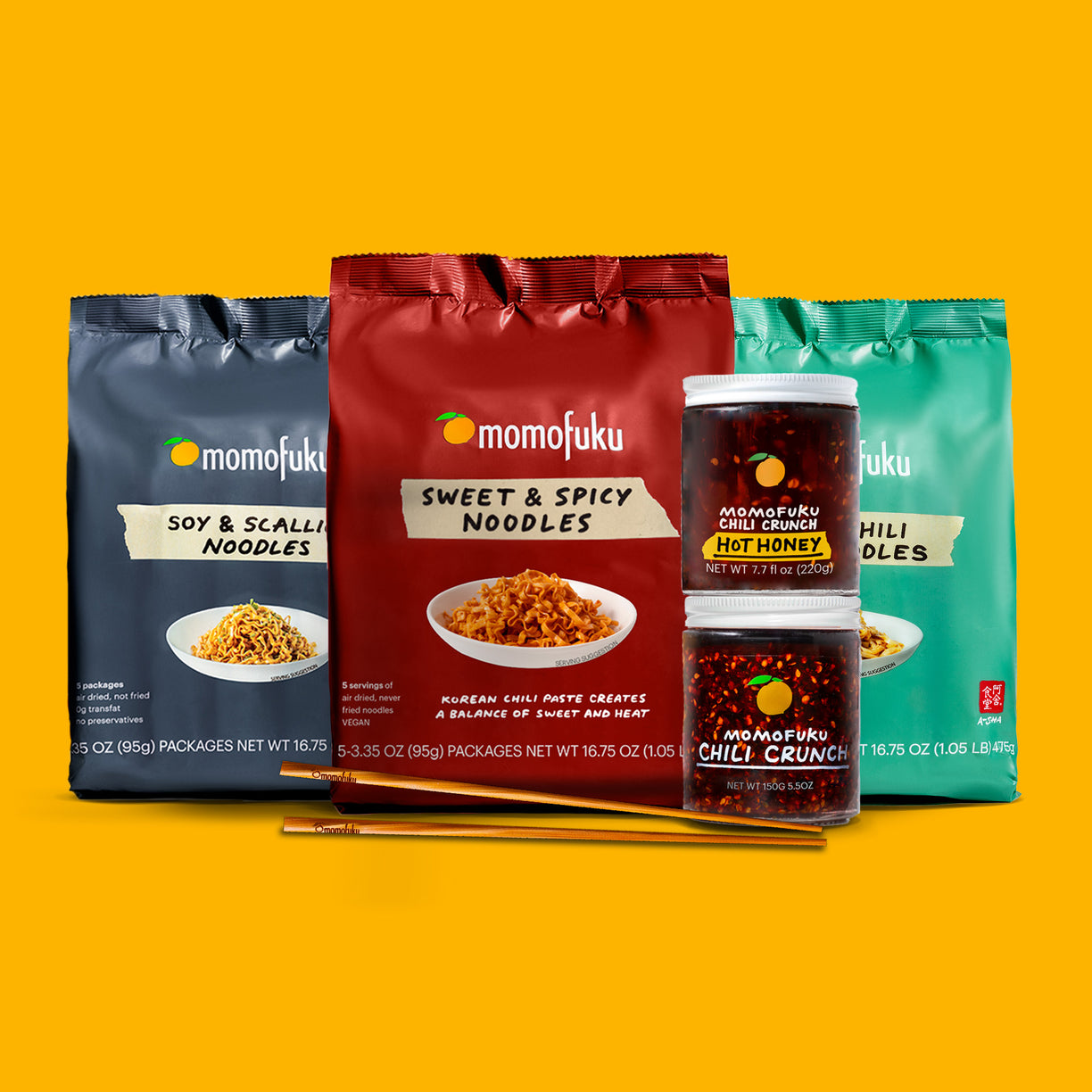 Assorted Momofuku noodle packs and chili crunch jars with chopsticks on a yellow background.