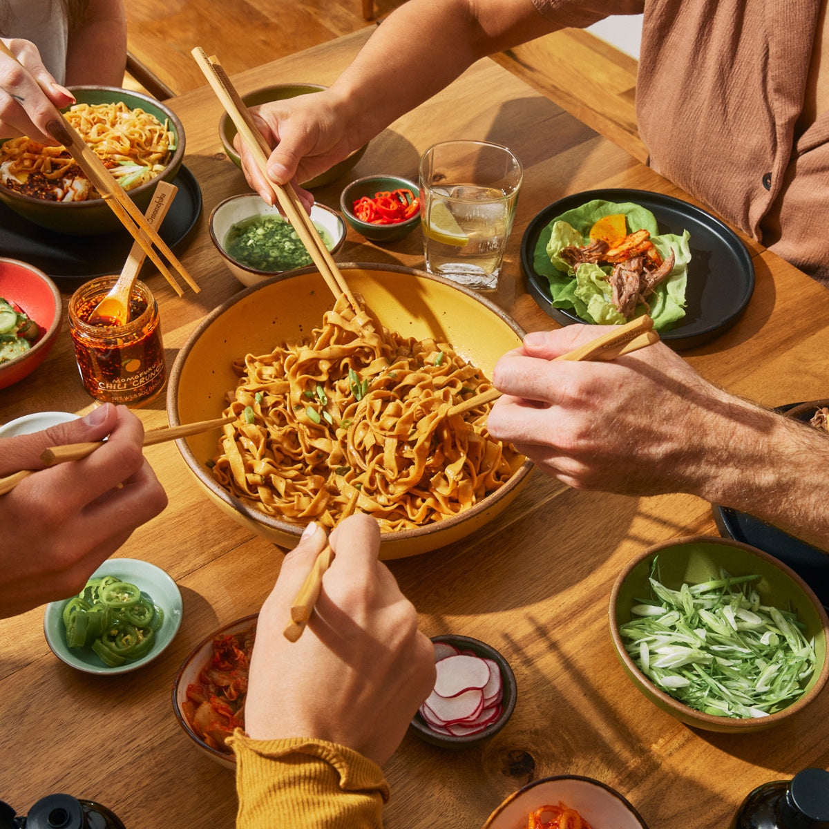 sharing a bowl of noodles with small plates and chili crunch