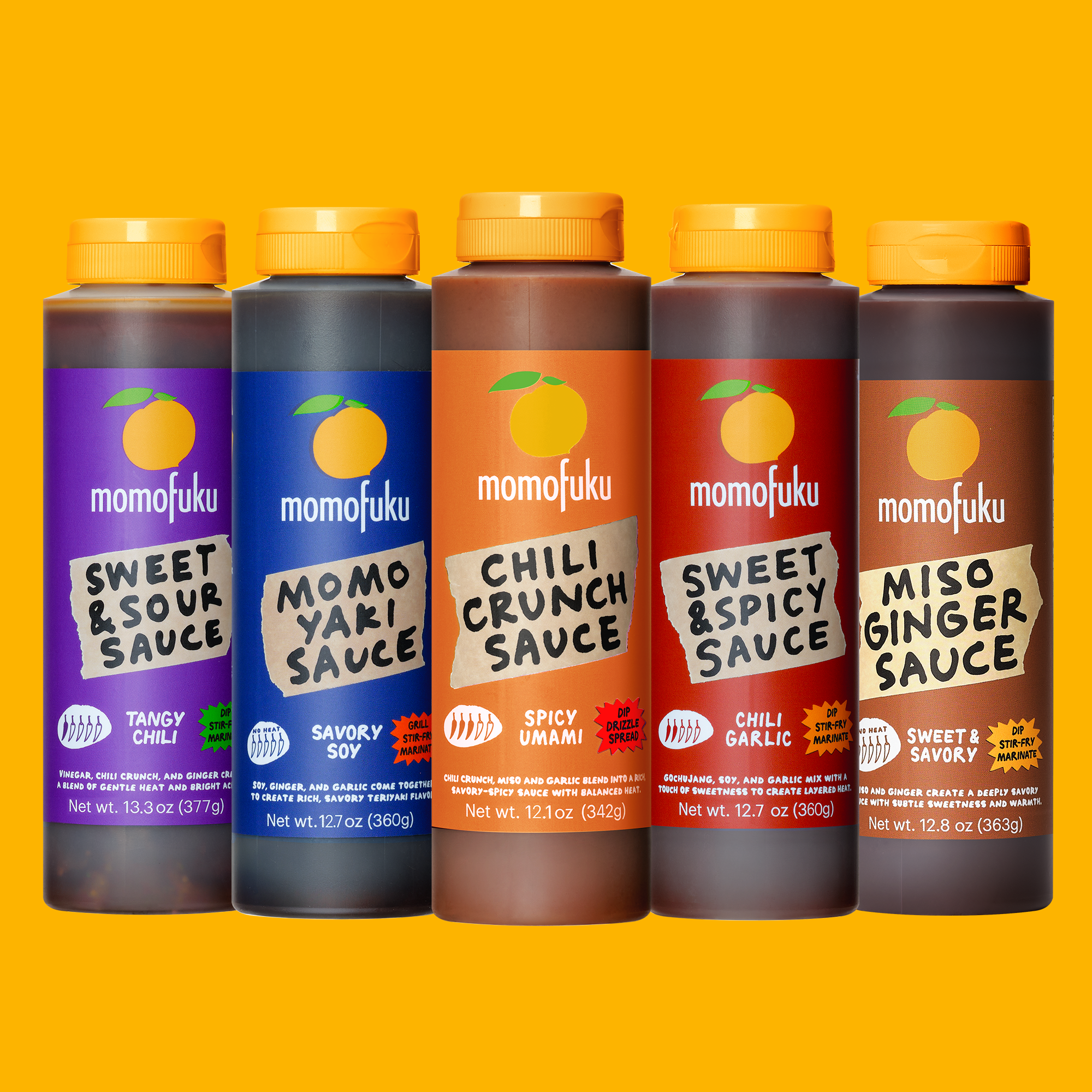 Five bottles of Momofuku sauce arranged side by side on a bright yellow background. The bottles are dark brown with orange caps and feature colorful labels for Sweet & Sour Sauce, Momoyari Sauce, Chili Crunch Sauce, Sweet & Spicy Sauce, and Miso Ginger Sauce.