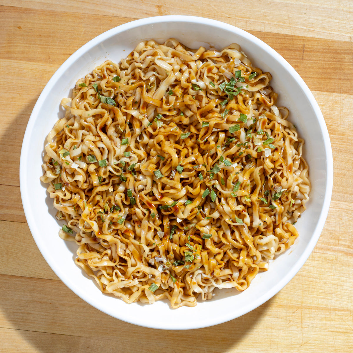 A bowl of seasoned stir-fried noodles with chopped green garnish.