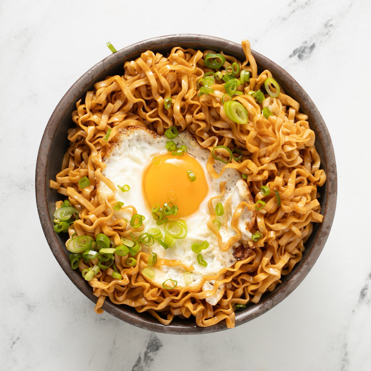 Bowl of noodles topped with a fried egg and scallions.